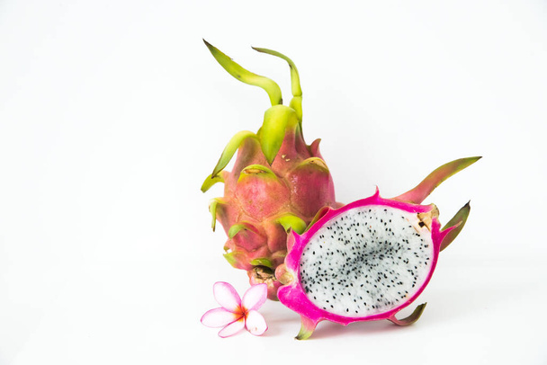 Fruto de dragón entero y medio junto con una flor de plumeria rosa sobre un fondo blanco
. - Foto, imagen