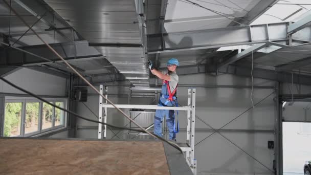 Trabajador de construcción masculino caucásico que fija las piezas del eje de aire acondicionado instalado en el techo del edificio nuevo
.  - Metraje, vídeo