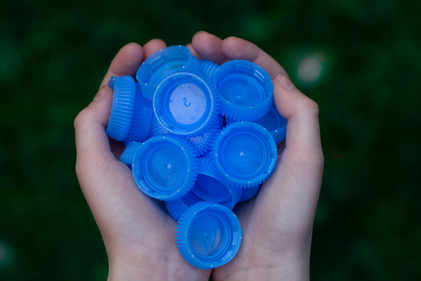 Mains d'enfant tenant des bouchons de bouteille en plastique bleu. Écologie et pollution de la planète Terre. Concept de recyclage. - Photo, image