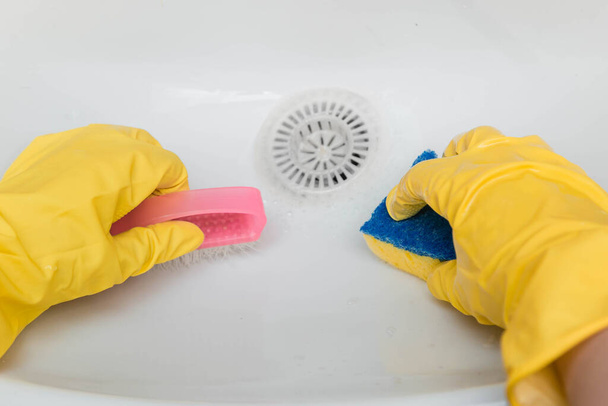 Vista em primeira pessoa, close-up de mãos em luvas de borracha amarela limpando a pia com uma esponja e uma escova
. - Foto, Imagem
