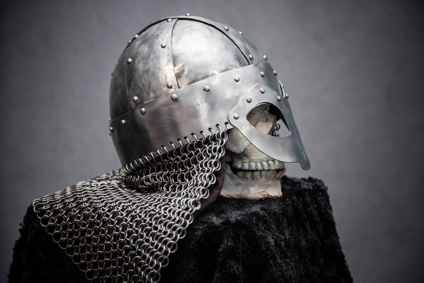 Crânio em um capacete Viking, em um suporte preto, em um fundo cinza
 - Foto, Imagem