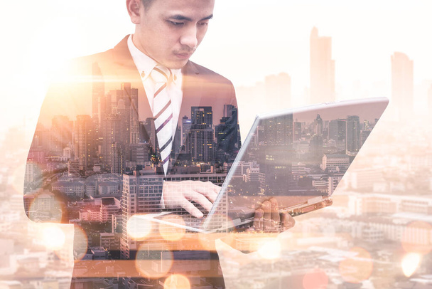 The double exposure image of the business man using a laptop computer during sunrise overlay with cityscape image. The concept of modern life, business, city life and internet of things. - Foto, Imagem