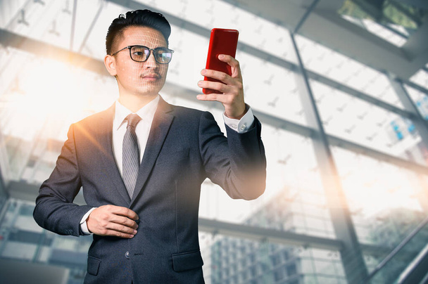 asiatischer Geschäftsmann hält Smartphone auf modernem Stadthintergrund - Foto, Bild