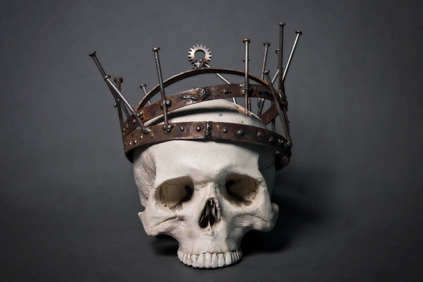 A human skull in a rusty crown, made of nails, gears and metal bands. A photo on a gray background. Postapocalypse, industrial style. - Foto, Imagem