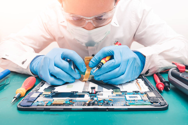 The abstract image of the technician repairing inside of tablet by screwdriver in the lab. the concept of computer hardware, mobile phone, electronic, repairing, upgrade and technology - Photo, Image