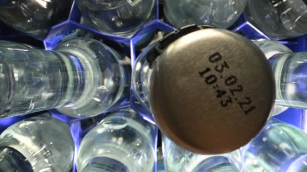 Pohled na čiré skleněné láhve naplněné vodou a kovovými uzávěry s datem spotřeby organizované v plastové nádobě. Osoba Volba a uchopení jedné z lahví.  - Záběry, video