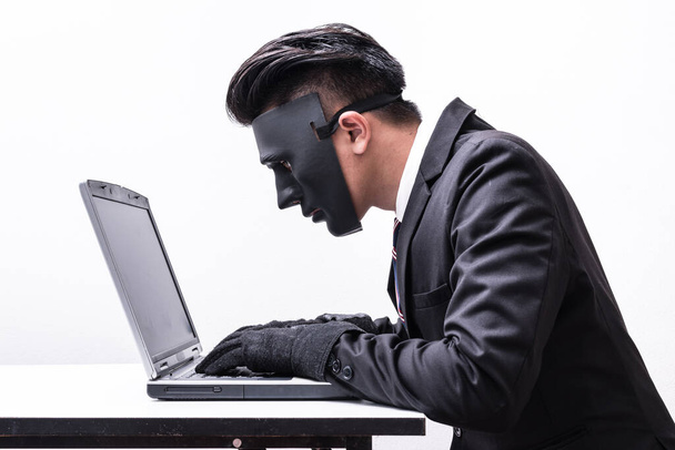 The abstract image of the hacker or programmer wear a mask using a laptop in the empty white room. the concept of cyber attack, virus, malware, illegally and cyber security. - Photo, Image