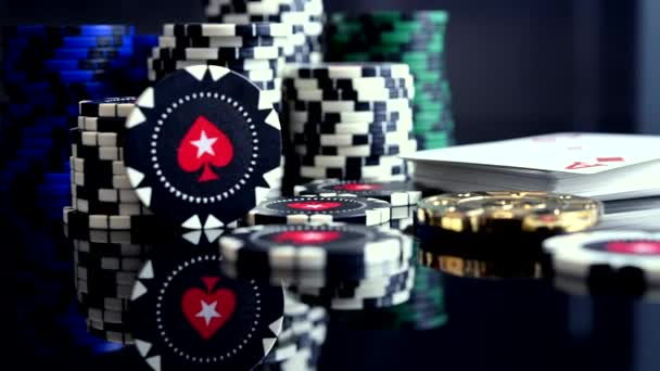 Hromada barevných žetonů pro kasino a balíček hracích karet s eso na vrcholu na černém skleněném stole s reflexí.  - Záběry, video
