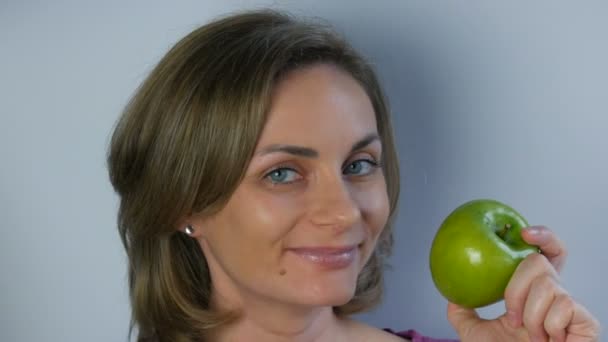 Arckép egy fiatal, gyönyörű nőről, aki nagy zöld almákat tart a kezében, elgondolkodva mosolyogva. A vegán és az étrend fogalma, friss gyümölcs egy fiatal lány kezében, egészséges étel - Felvétel, videó