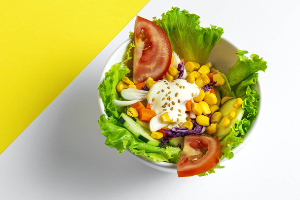 Homemade Fresh lettuce salad with tomatoes, red onion,corn, carrots, cucumber and sesame sauce on colors background from above. Healthy food. Vegan foood.  - Photo, Image