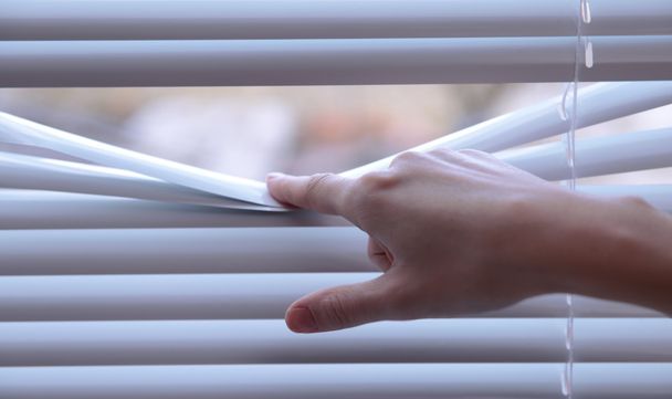 Female hand separating slats of venetian blinds with a finger to see through - Foto, Imagen