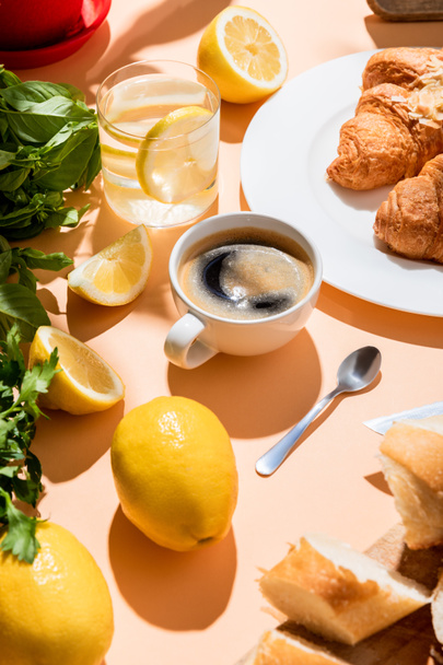 coffee, croissants, water with lemon for breakfast on beige table - Fotó, kép