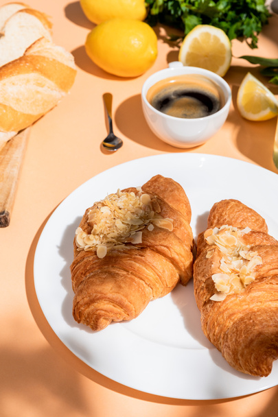 κρουασάν, μπαγκέτα, λεμόνια και φλιτζάνι καφέ για πρωινό σε μπεζ τραπέζι  - Φωτογραφία, εικόνα