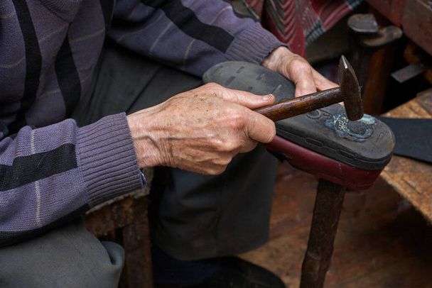 Pensioner repairs shoes at home. In one hand holds a hammer, in the other hand a shoe. Horizontal frame. - Photo, Image