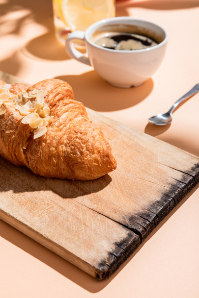 fresh croissants on cutting board and cup of coffee for breakfast on beige table - Fotó, kép