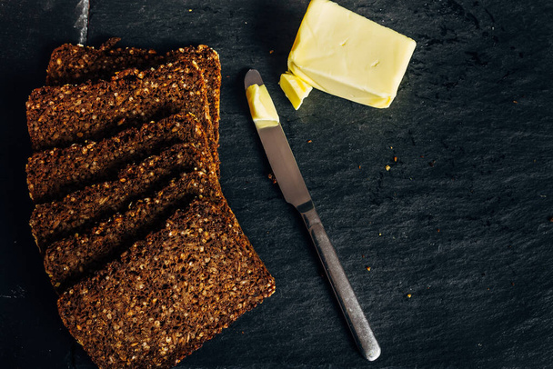 pain de seigle pain grillé au beurre dans les aliments sombres avec couteau en métal, concept de nourriture saine et petit déjeuner exquis
 - Photo, image