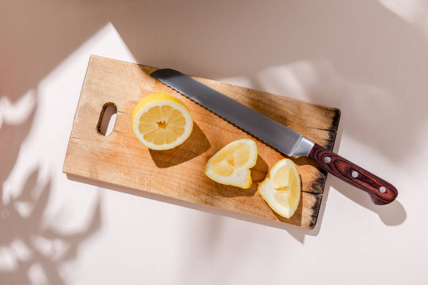 top view of cutted lemon on wooden board with knife on grey table with shadows - 写真・画像