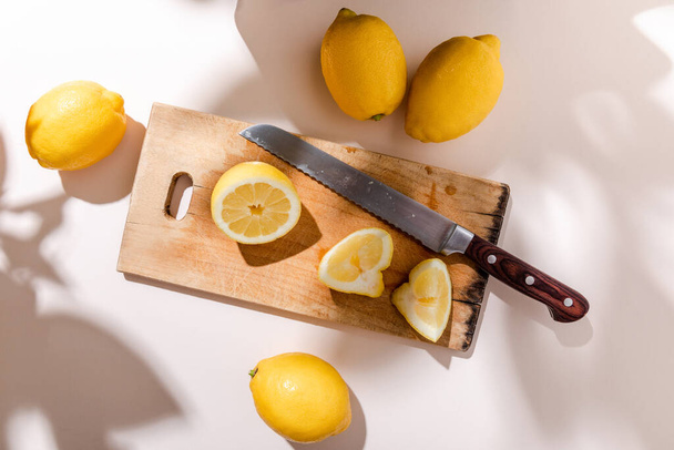 whole and cutted lemons on wooden board with knife on grey table - Фото, изображение
