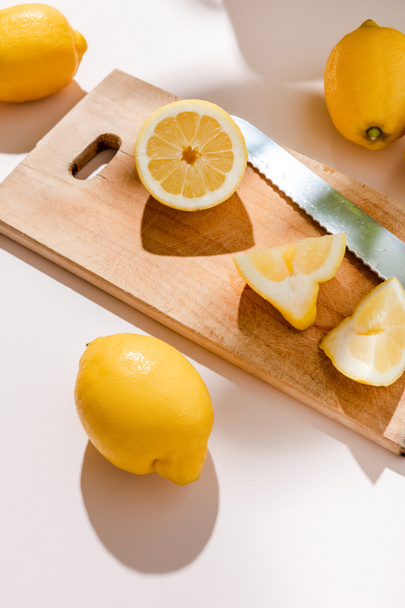 fresh whole and cutted lemons on wooden board with knife on grey table  - Fotoğraf, Görsel