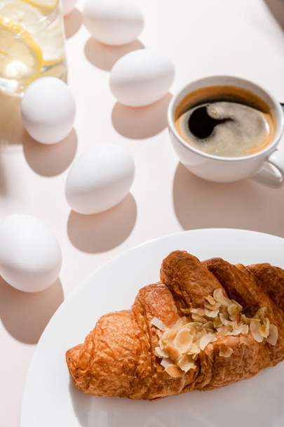 tojás, croissant, kávé és citromos víz reggelire szürke asztalon árnyékokkal - Fotó, kép