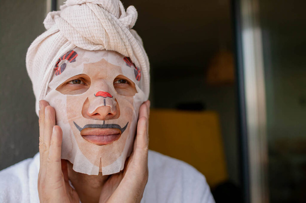 Young Man Doing Facial Mask Sheet. Beauty And Skin Care Concept - Photo, Image