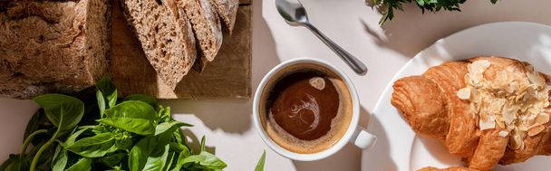 top view of fresh croissants, bread, basil and cup of coffee for breakfast on grey table, website header - Photo, Image