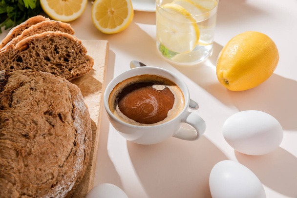 bread, eggs, lemon water and cup of coffee for breakfast on grey table  - Foto, imagen