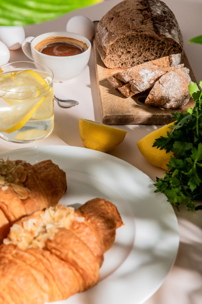 verse croissants, brood, eieren, koffie en citroenwater voor ontbijt op grijze tafel, selectieve focus - Foto, afbeelding