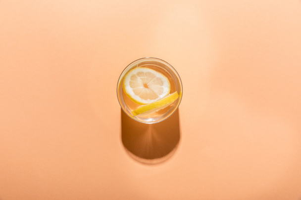 top view of fresh water with lemon slices in glass on beige with shadow - Foto, imagen