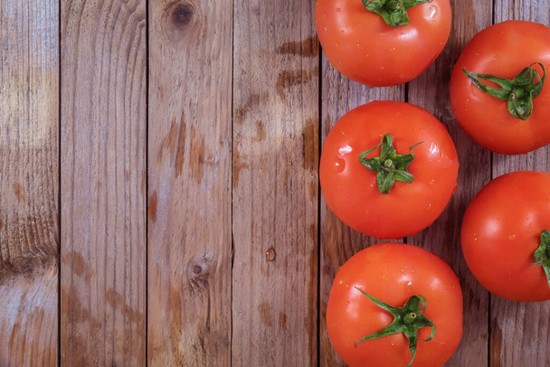 On a wooden table there are fresh tomatoes in the amount of five pieces. They are ripe, round, small. Tomatoes photographed from above - Foto, Imagen