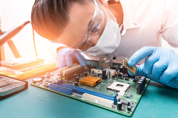 The asian technician is putting the CPU on the socket of the computer motherboard. the concept of computer hardware, repairing, upgrade and technology. - Photo, Image