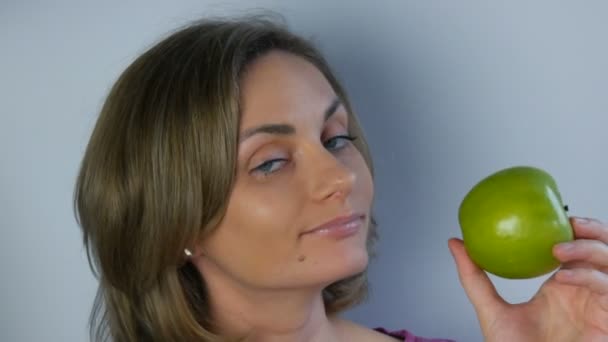 Obličej mladé krásné ženy s velkými zelenými jablky v rukou, zamyšleně se usmívající. Pojem vegan a strava, čerstvé ovoce v rukou mladé dívky, zdravé jídlo - Záběry, video
