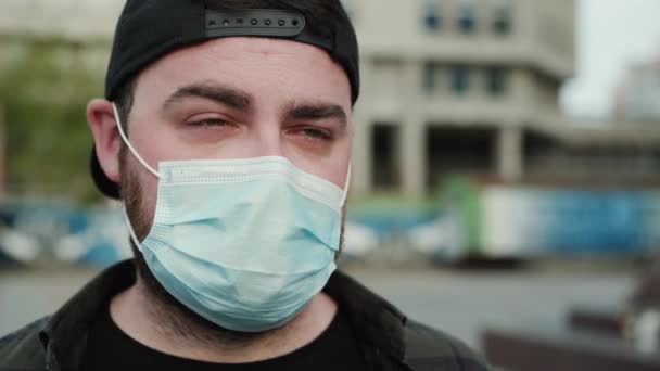 Portrait of young man in medical mask looks into camera with teary eyes - Video, Çekim
