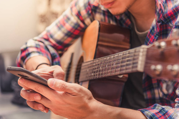 The man playing the guitar in the bright room. The man try to learning the guitar lesson from the internet with his smart phone. - Foto, Imagem