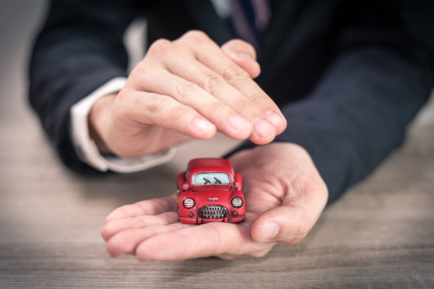 The abstract image of the asian business man hold a toy car on the table. The concept of automobile, property, ownership, insurance and transportation. - Фото, изображение