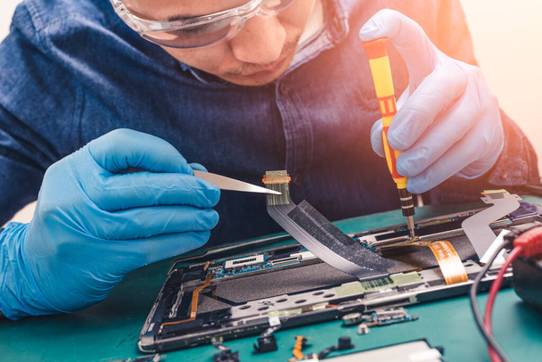 The abstract image of the asian technician repairing a tablet by screwdriver in the lab. the concept of computer hardware, mobile phone, electronic, repairing, upgrade and technology. - Foto, Imagem