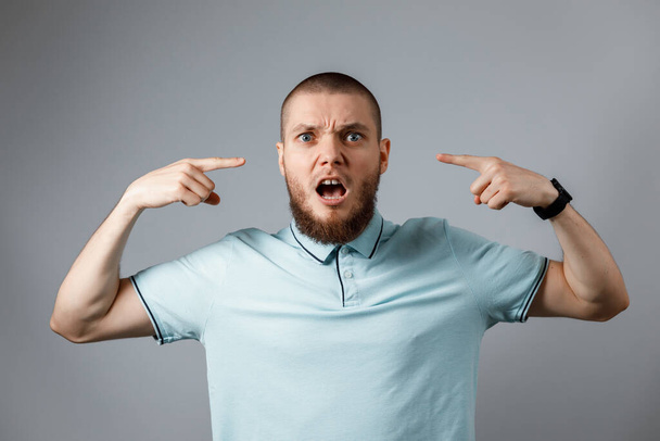 Muotokuva nuoresta miehestä sinisessä t-paidassa vihaisena huutamassa harmaalla taustalla. eristetty - Valokuva, kuva