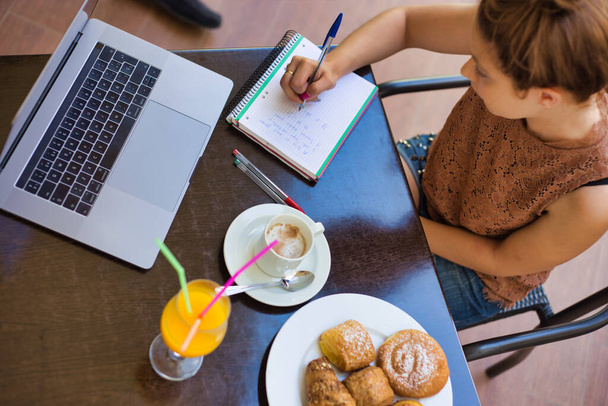 Légi felvétel egy nőről, aki egy teraszon ül, és egy laptopon dolgozik gyümölcslével és pékséggel az asztalon - Fotó, kép