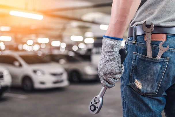 The abstract image of the back of technician hold a wrench and blurred garage is backdrop. the concept of automotive, repairing, mechanical, vehicle and technology. - Photo, image