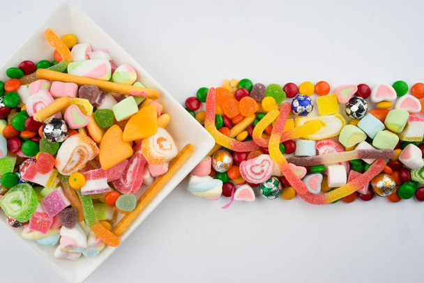 Kreatywny układ kolorowych cukierków i słodyczy na białym tle. Widok płaski. - Zdjęcie, obraz