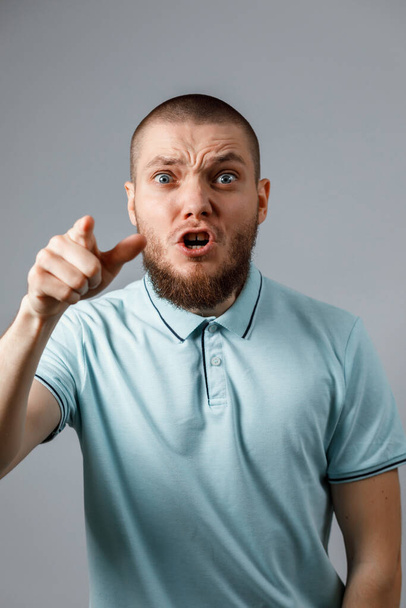 Portré egy kék pólós fiatalemberről, aki dühösen kiabál a szürke háttér fölött. izolált - Fotó, kép