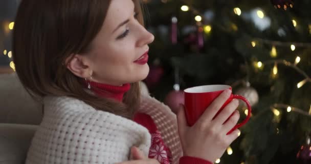 Mujer agradable bebiendo café por árbol de Navidad
 - Imágenes, Vídeo