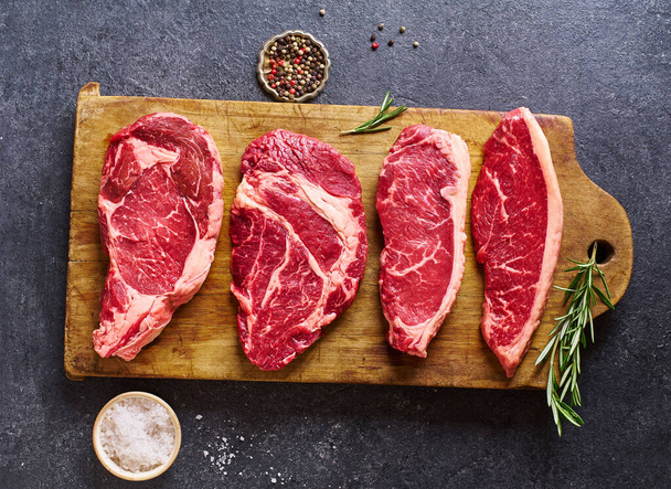 cutting board with ribeye and striploin with picanha and chuck roll  fresh black angus prime raw beef steaks on wooden background, top view - Photo, Image