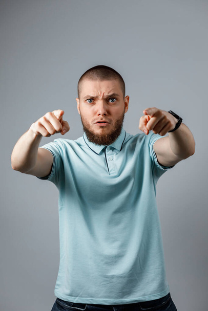 Πορτρέτο ενός νεαρού άνδρα με μπλε μπλουζάκι θυμωμένος φωνάζοντας πάνω από ένα γκρι φόντο. απομονωμένα - Φωτογραφία, εικόνα