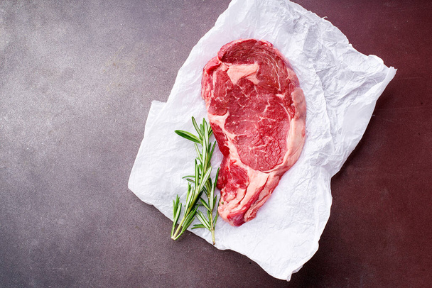 Black Angus prime beef rib eye steak ready for barbecue on parchment paper with rosemary, Top view  - Фото, изображение