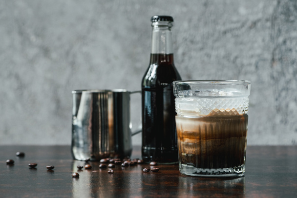 cold brew coffee with milk in glass near bottle, milk jug and coffee beans on wooden table - Foto, afbeelding