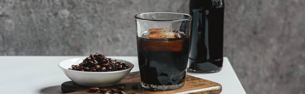 café frio brew com gelo em vidro e garrafa perto de grãos de café em tábua de corte na mesa branca, tiro panorâmico
 - Foto, Imagem