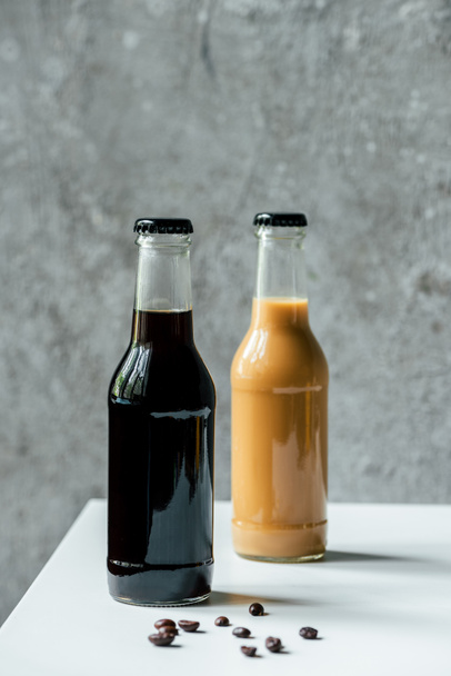 selective focus of cold brew coffee in bottles near coffee beans on white table - Foto, Imagem