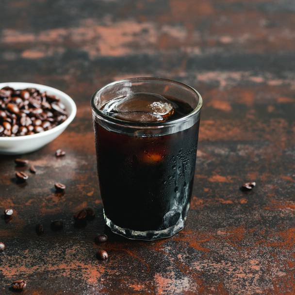 enfoque selectivo de café de cerveza fría con hielo en vidrio cerca de granos de café en la superficie oxidada
 - Foto, Imagen