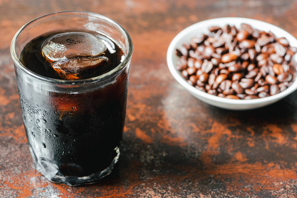 selective focus of cold brew coffee with ice in glass and bottle near coffee beans on rusty surface - Foto, afbeelding